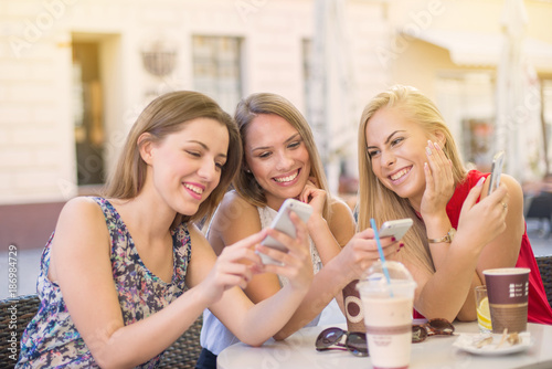three amazing womans talking and sharing miles while sitting on a outside coffee table in a turist city. Sharing selfies