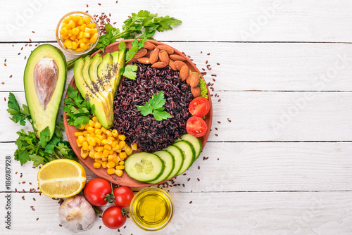 Black rice, avocado, cucumber, corn and almonds. On a wooden background. Top view. Free space for your text.