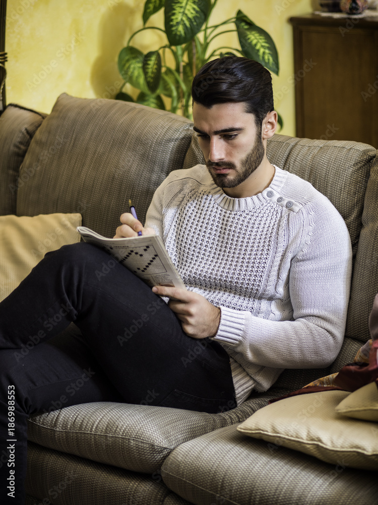 Young Man Sitting Doing A Crossword Puzzle Looking Thoughtfully At A 