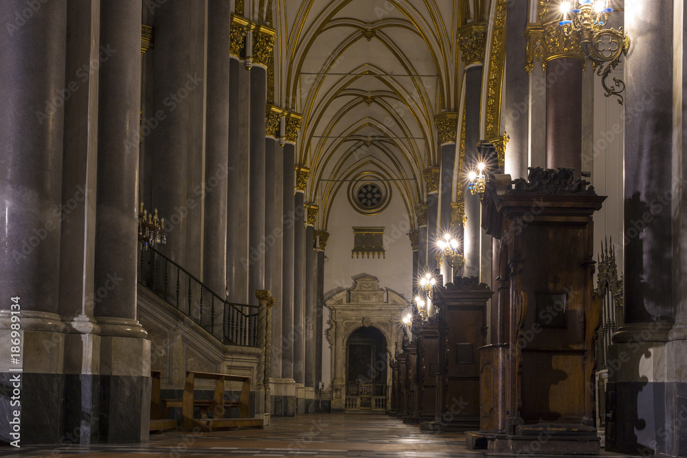 View in the side aisle of the Basilica of San Domenico Maggiore in Naples, Italy. There are tall columns in the church as well as confessionals and wooden benches.