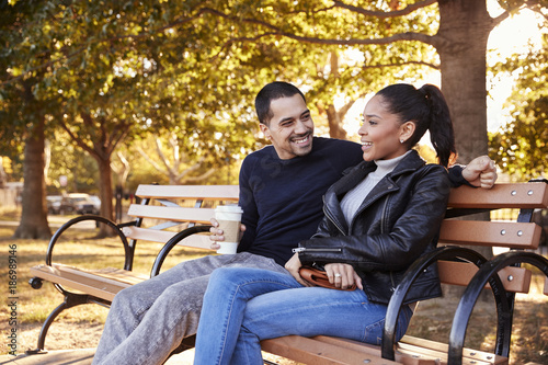 Young Hispanic couple sitting on bench in Brooklyn park