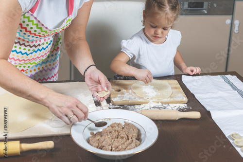 Little girl and mom make dumplings in the kitchen at home