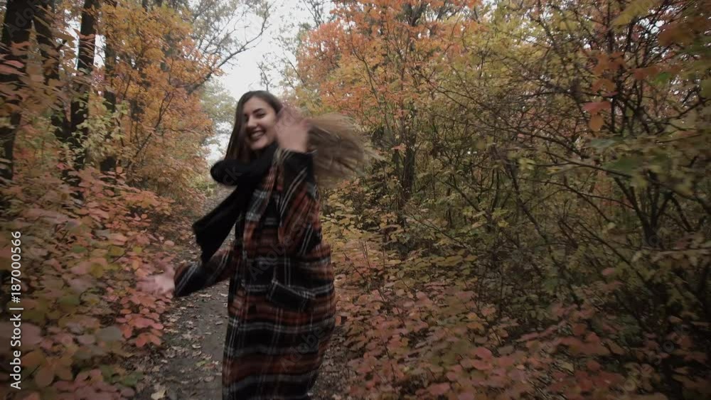 Young beautiful brunette girl running along the forest road. Autumn.