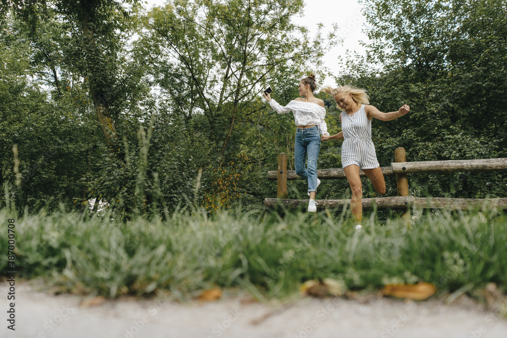 Two happy young women jumping from fence in a park Two happy young women jumping from fence in a park