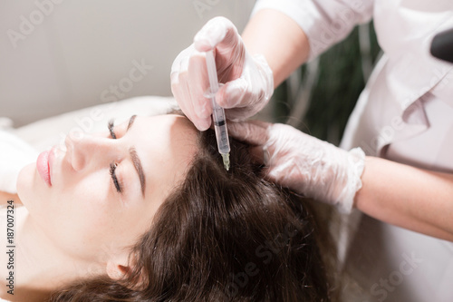 Handsome woman receives an injection in the head. The procedure makes doctor in white gloves. The concept of mesotherapy. Thrust to strengthen the hair and their growth