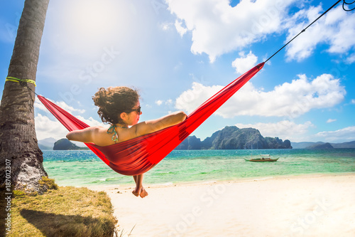 Young caucasian female relaxing in a red hammock on a tropical b