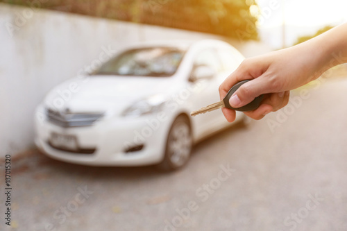 A hand of woman holding a car key cover blur car background.