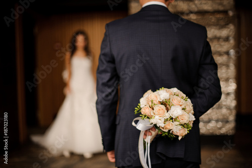 groom keeping behind a bouquet of roses waiting for bride