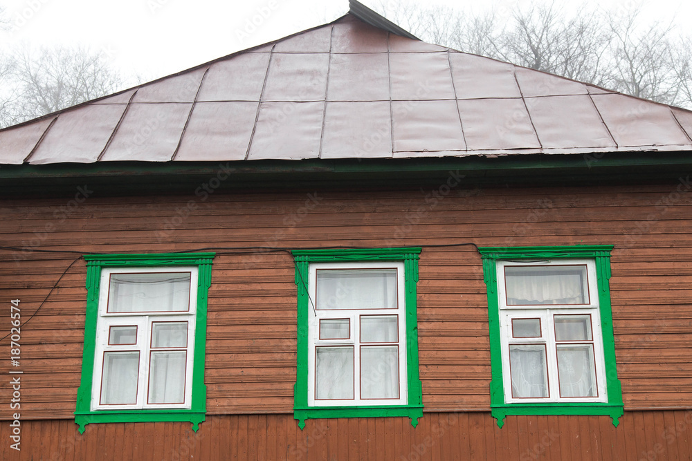 wooden house with three windows and a roof in the village