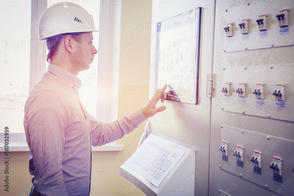 engineer controls technological process on control panel. Serviceman in white helmet monitors the technical indicators on display of automated system.