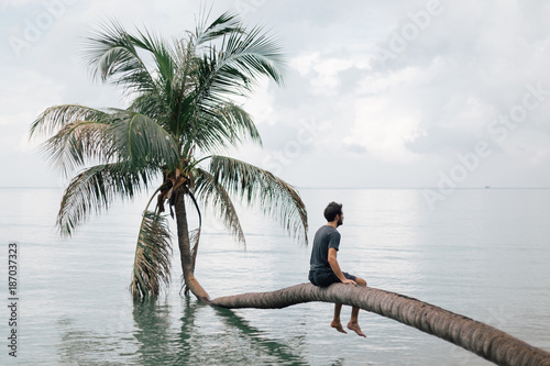 Young man sitting on the coconut tree over the sea photo