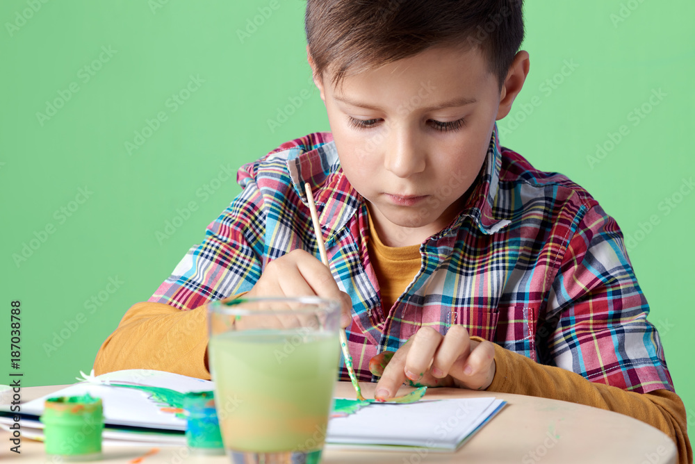 Caucasian boy is carefully painting with watercolors. Caucasian boy is carefully painting with watercolors.