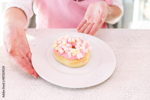 Female hands holding plate with pink donut on on white wooden background