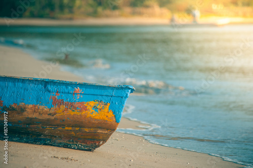 Colorful wooden fishing boat on sand beach with sea wave in the background in vintage style. (Soft focus)