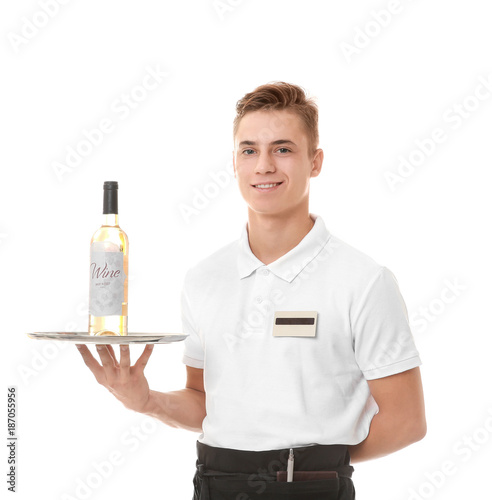 Handsome young waiter holding metal tray with bottle of wine on white background