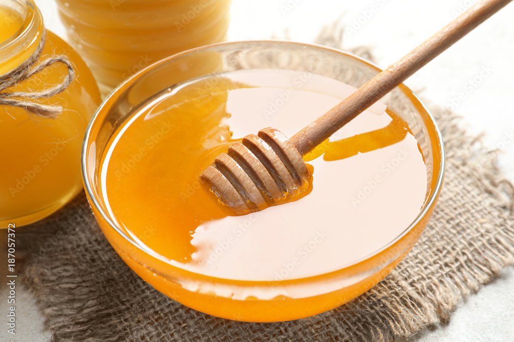 Glass bowl with delicious honey and dipper on table, closeup