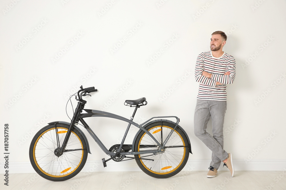 Handsome young hipster man with bicycle near light wall Handsome young hipster man with bicycle near light wall