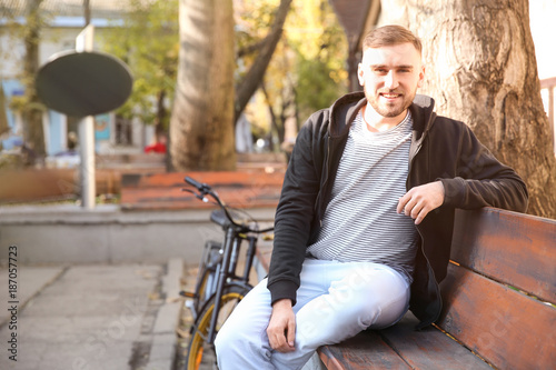 Handsome young hipster man with bicycle sitting on bench outdoors