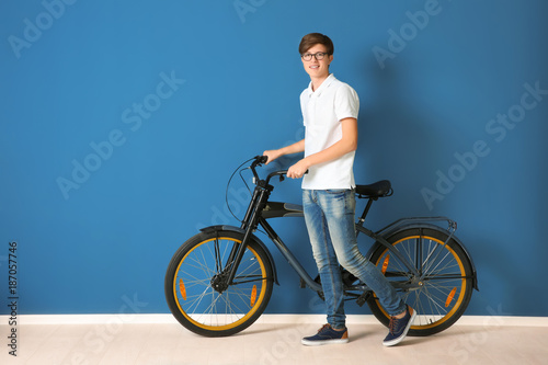 Hipster teenager with bicycle on color background