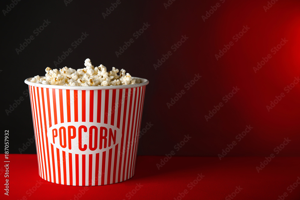 Striped bucket with tasty popcorn on table against dark background