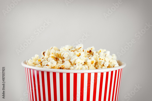 Striped bucket with tasty popcorn on light background, closeup