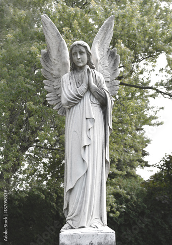 Vintage sad angel on a cemetery against the trees and leaves background. Holy angel.