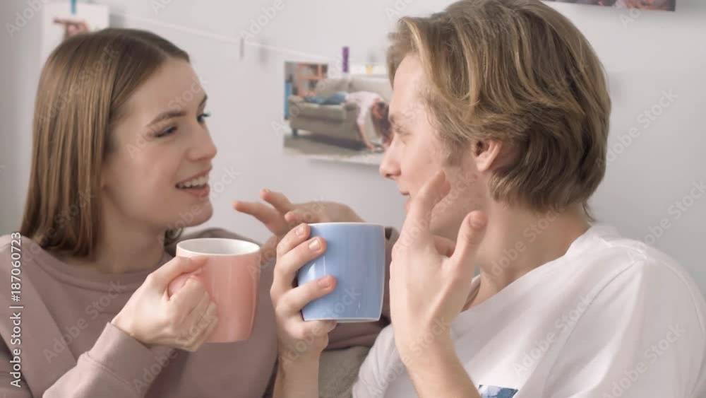Two attractive belovers on the frontground holding colorful cups. Having coffee discuss their winter holidays. Two attractive belovers on the frontground holding colorful cups. Having coffee discuss their winter holidays.