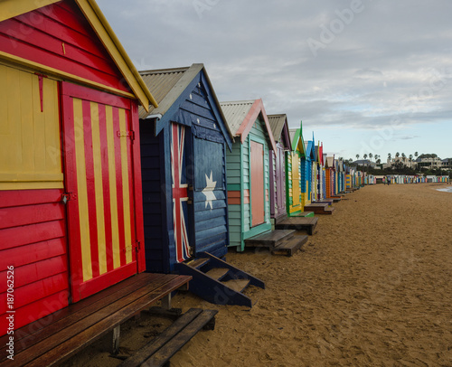 Colourful beach boxes line the Brighton shoreline in Australia  featuring the Australian flag prominently.