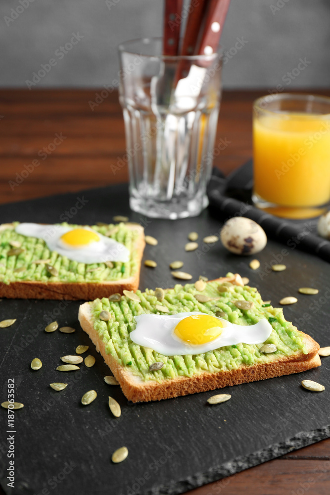 Tasty toasts with avocado paste and fried quail egg on slate plate