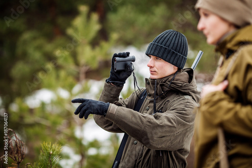 male and woman hunters ready to hunt, holding gun and walking in forest.