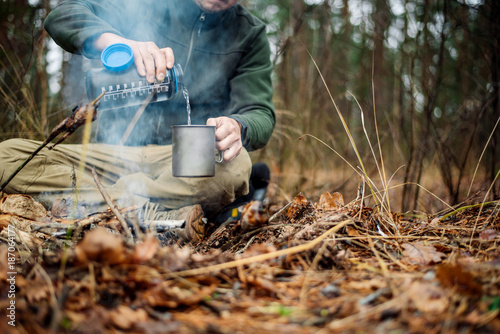 hunter pours water from a bottle into a metal mug. bushcraft, adventure, travel, tourism and camping concept.