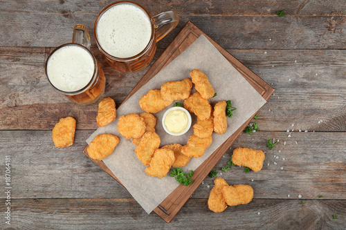 Tasty chicken nuggets, beer and sauce on table