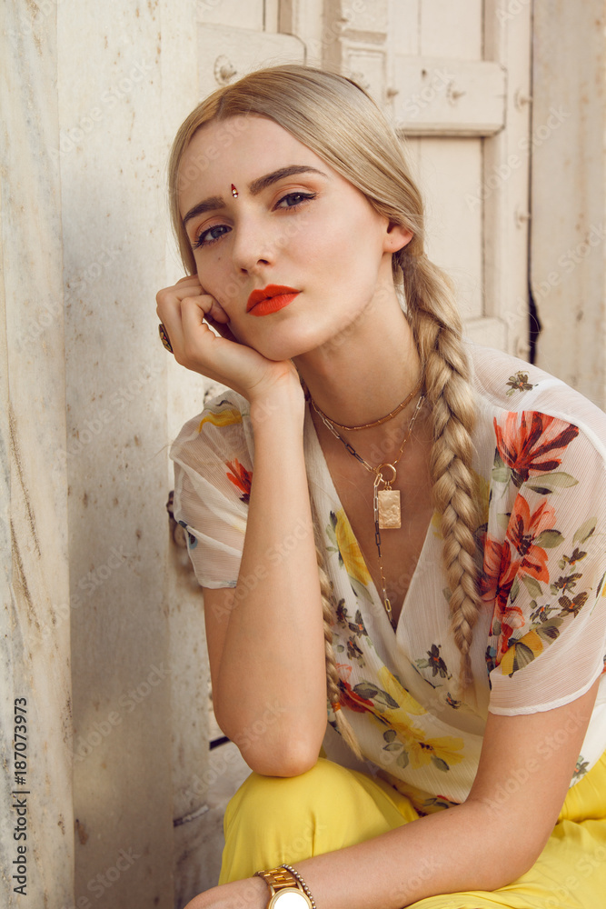 Fototapeta premium Close-up portrait of a beautiful young woman with a gorgeous bindi on her forehead. Long blonde hair is tangled. She is dressed in a pretty shirt with floral print and yellow skirt