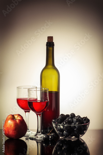 Still life with red wine / A bottle of red wine, two glasses, an apple, and a cup with grapes standing on a table