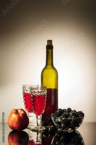 Still life with red wine / A bottle of red wine, two glasses, an apple, and a cup with grapes standing on a table