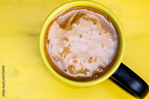 Coffee in a black mug on a yellow wooden background
