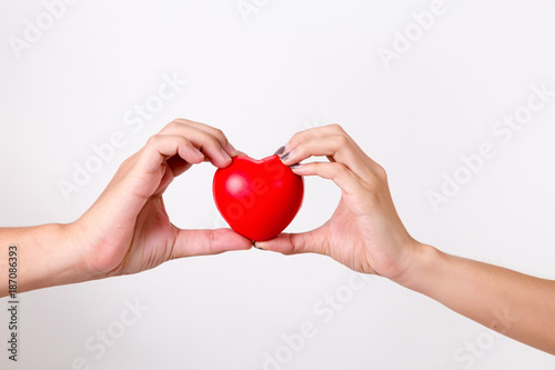 Man's hand and woman's hand holding a red heart.  Isolated on white background. Studio lighting.
