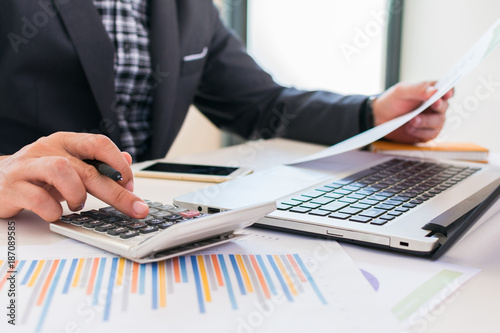 Businessman working with calculator  Business document and laptop computer notebook. Businessman is reading the report and analyzing graph report.