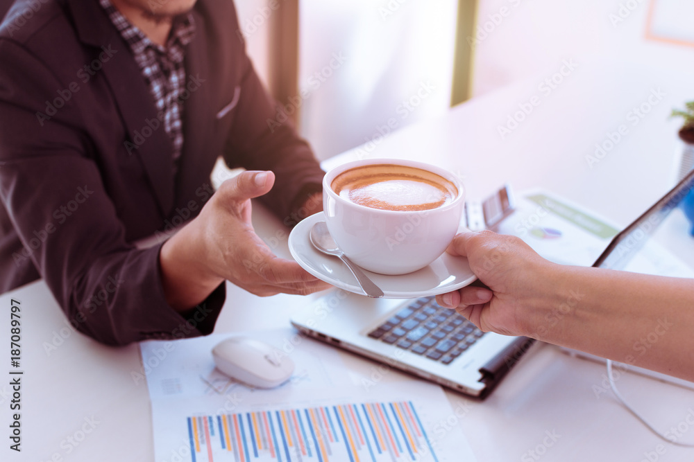 Close up of man's hand taking coffee cup from woman's hand in coffee shop. Portrait of hand holding white cup of cappuccino in office or co-workspace. Close up of man's hand taking coffee cup from woman's hand in coffee shop. Portrait of hand holding white cup of cappuccino in office or co-workspace.