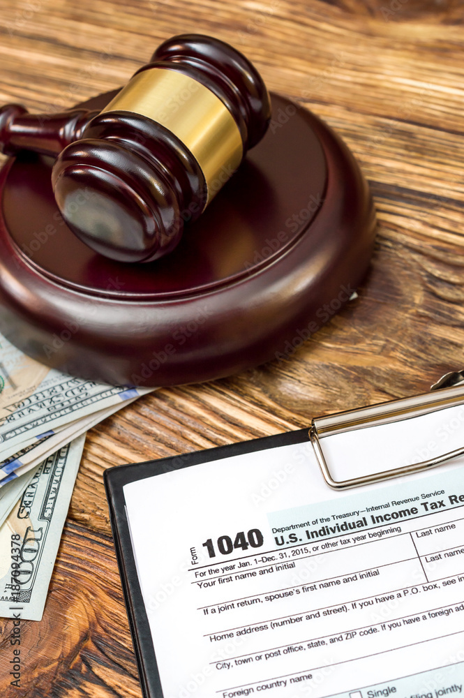 Tax form on clipboard with money and judge's gavel on the table.