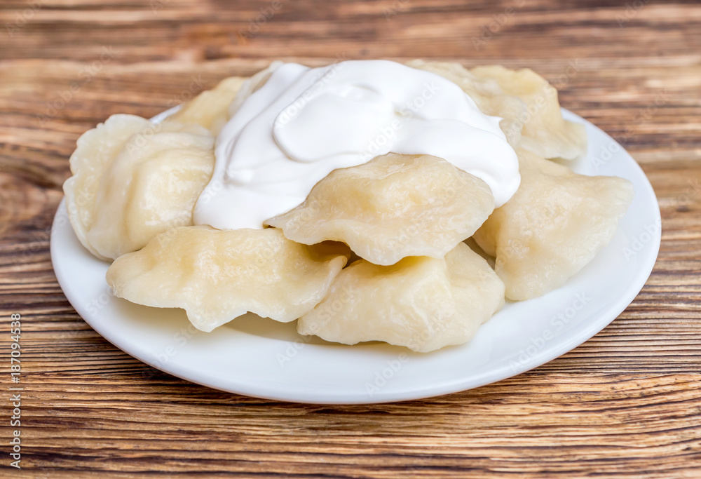 Plate with boiled varenyky and sour cream on wooden table. Plate with boiled varenyky and sour cream on wooden table.