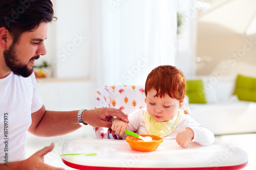 father teaches son, baby to hold the spoon and eat by his own