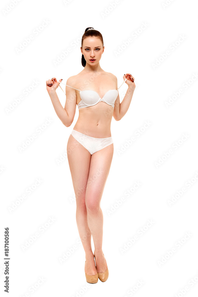 A young woman stands in her underwear and holds the bra strap straps.  Isolated on white background. Stock Photo