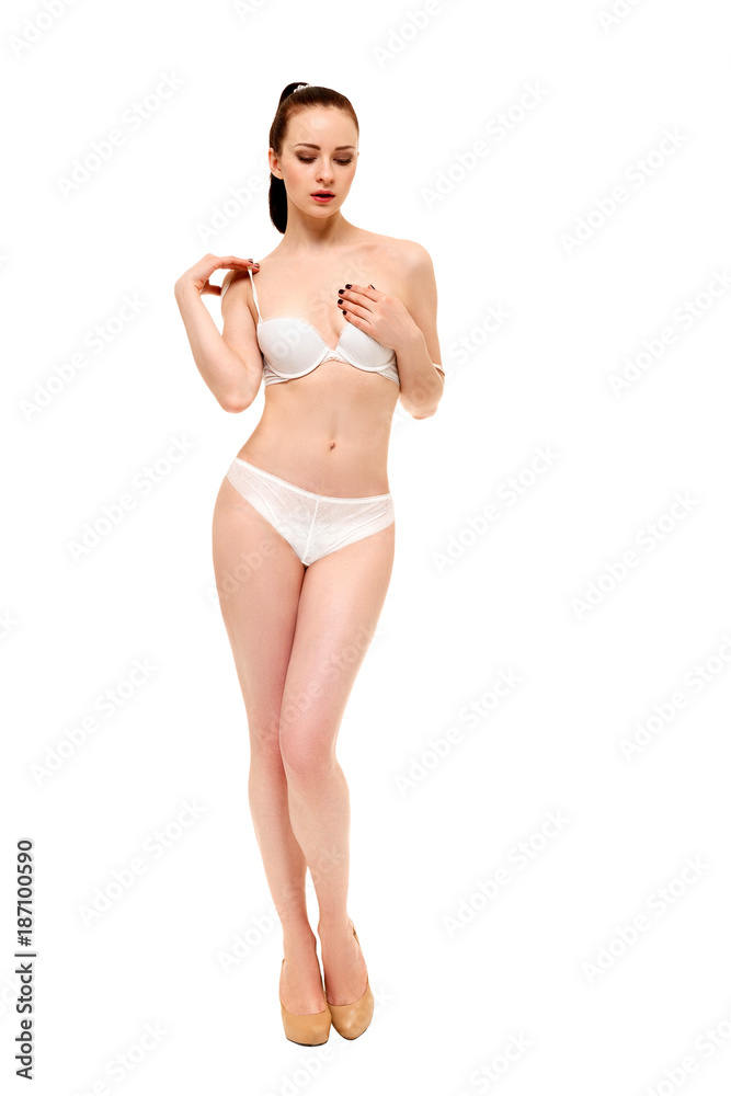 A young beautiful woman takes off a bra, covering her breast with her hand.  Isolated on white background. Stock Photo