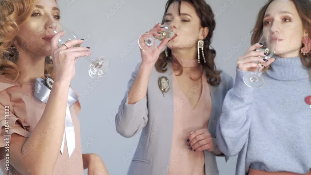 Three girls having fun, dancing and drinking white wine or champagne from glass goblets in studio on white background Three girls having fun, dancing and drinking white wine or champagne from glass goblets in studio on white background