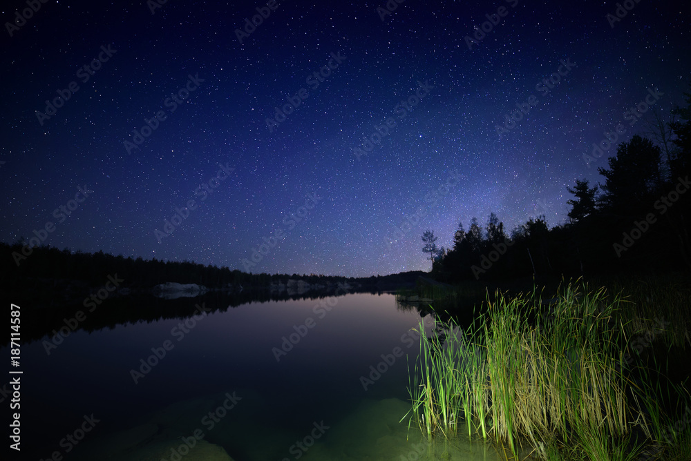 Lake at night with amazing starry sky and reflections in the water. Natural outddors travel dark background.