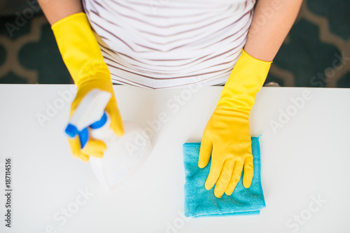 The young woman in yellow gloves holding rag and window cleaner in hands indoors