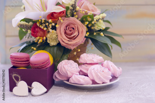 Romantic festive compositions with flower basket and sweets- a plate of marshmellows and a box of macaroons agains a light colored wooden background.St. Valentines, anniversary, wedding concept