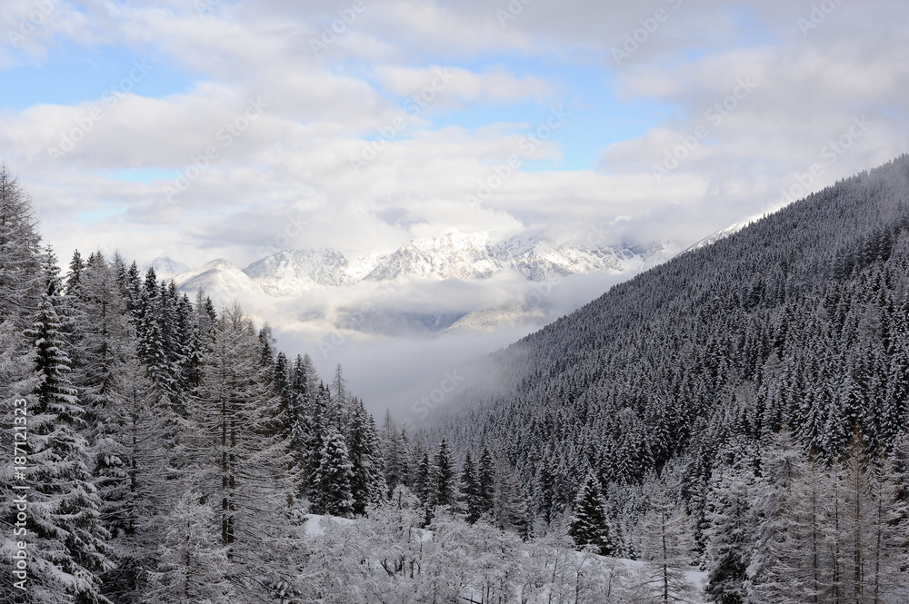 Panorama of Austrian Stubai Alps with mountain ranges and trees covered in snow and blue sky and clouds in winter