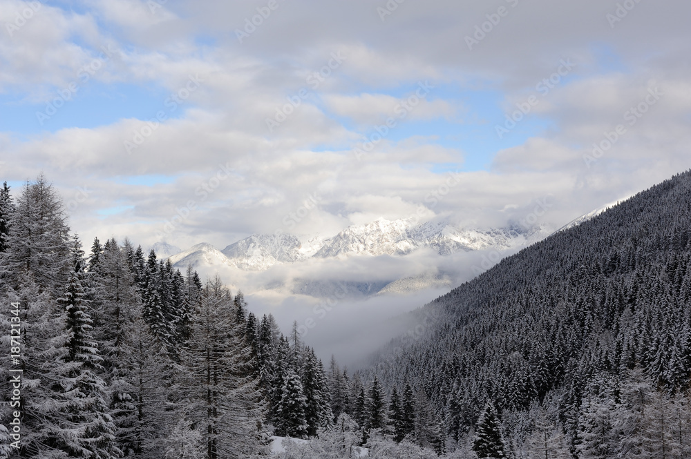 Panorama of Austrian Stubai Alps with mountain ranges and trees covered in snow and blue sky and clouds in winter